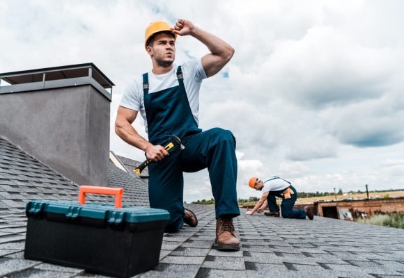 selective focus of handsome handyman touching helmet while holding hammer